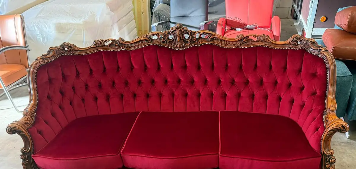 Driezits barokbank met een gesneden houten lijst, zitting en rug opnieuw bekleed in rood velours met capitonnage.