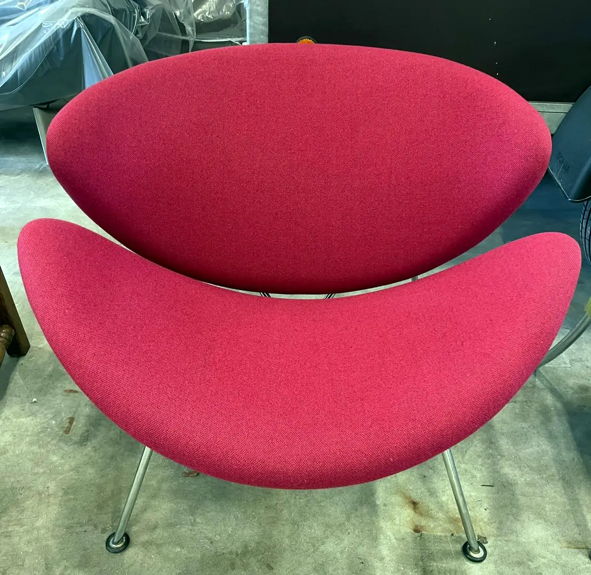 Designfauteuil met twee schelpvormige delen in rode stof op dunne stalen poten.