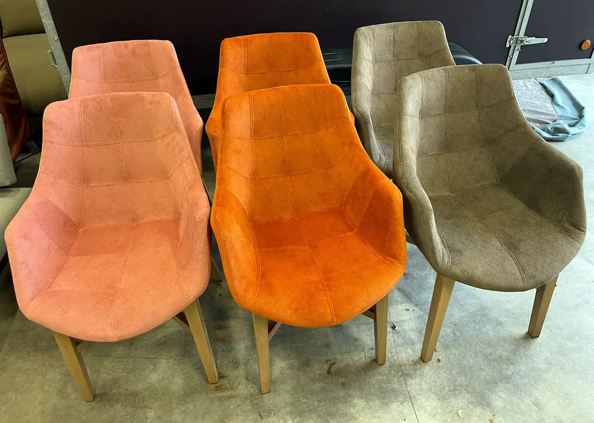 Zes eetkamerstoelen met houten poten, bekleed in velours in drie kleuren: roze, oranje en taupe.
