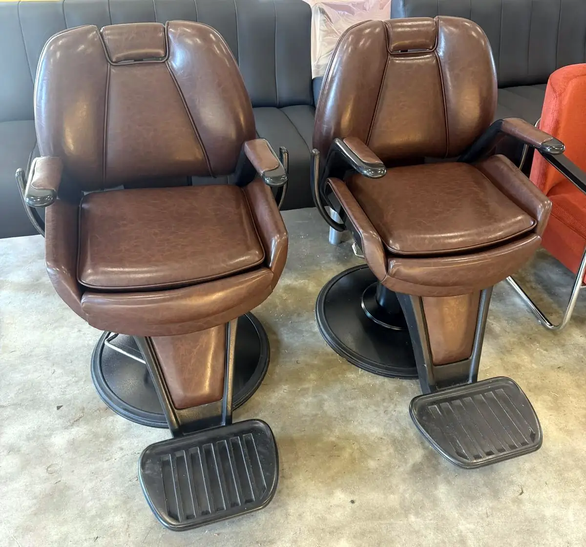 Twee kappersstoelen met voetsteun, opnieuw bekleed in bruin leer.