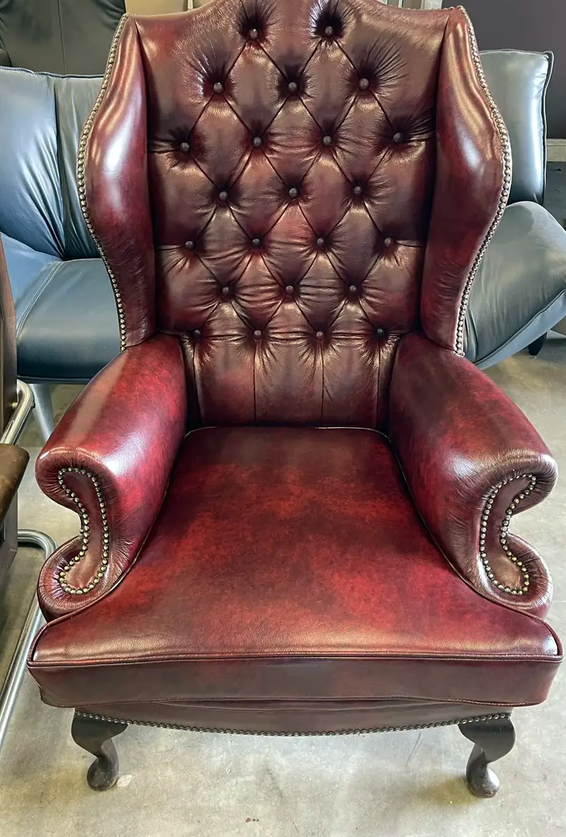 Klassieke oorfauteuil in bordeauxrood leer met diepe knoopcapitonnage, siernagels en gebogen houten poten.