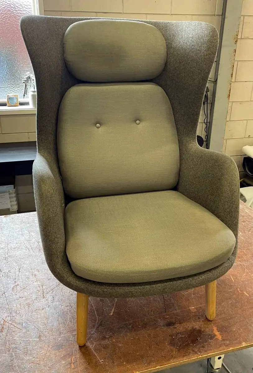 Moderne oorfauteuil met hoge rug in grijze stof, met knopen in de rug en houten poten.